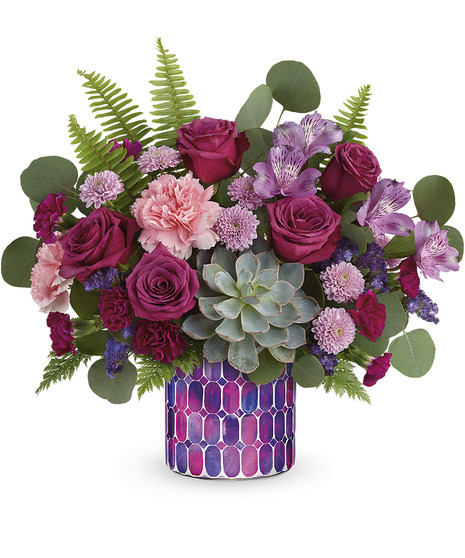 Purple alstroemeria, mini carns, pink carns, lavender buttons and purple statice are arranged with succulent plant , fern, and eucalyptus. in pink mosaic cylinder