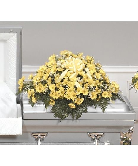 A casket piece with yellow daisies, white monte casino or baby's breath and leather leaf with bright yellow bow in the center.  Shown sitting atop a casket