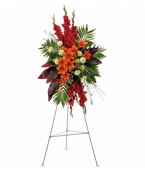 standing spray with orange lilies, red gladiola and ti leaves, green carnations and emeral and jade on green easel