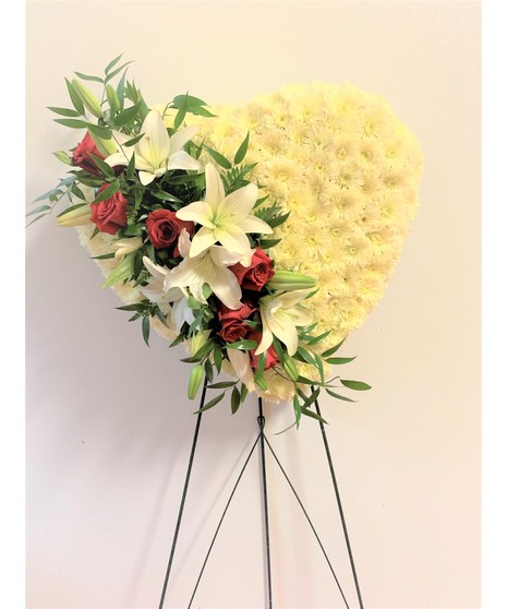 solid white heart on green metal easel with lilies, spray roses and ruscus going through a side representing a broken heart