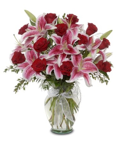 red roses pink stargazer lilies with lemon leaf and fern arranged compact in clear glass vase with ribbon on neck