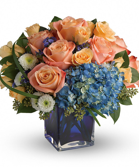 cobalt blue cube with blue hydrangea, peach roses and spray roses, white buttons, purple statice, lily grass, seeded eucalyptus, salal to create low compact round arrangement