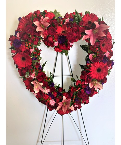 open heart on metal easel with red roses, gerbera, spray roses. purple lisianthus and statice, pink lilies, mini carnations. with leatherleaf 