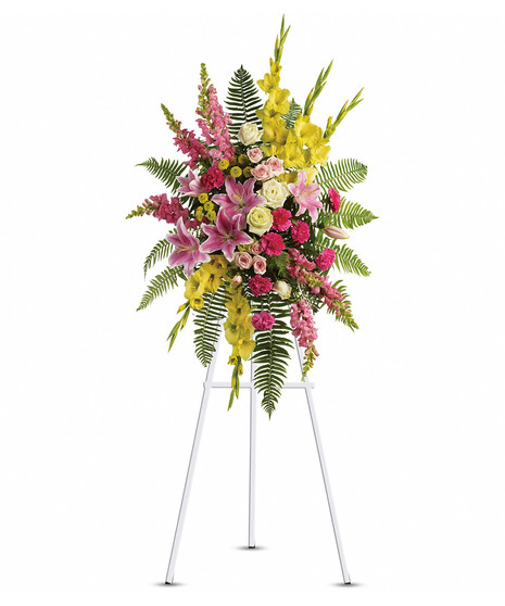 standing spray on green easel with yellow gladiola & buttons, pink snapdragons, carnations, spray roses and stargazer lilies and white roses amid sword fern and leather leaf