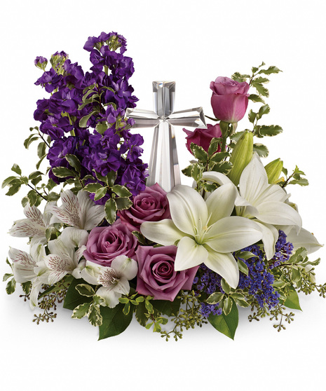 a beautiful heavy glass cross in center surrounded by purple stock, white liles & alstroemeria, lavender roses and variegated pittosporum make a wonder gif