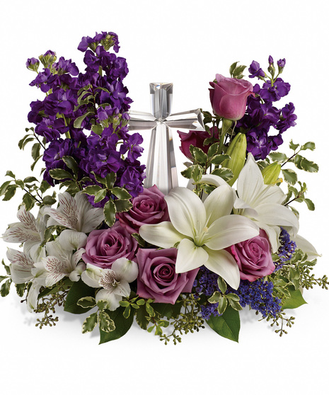 a beautiful heavy glass cross in center surrounded by purple stock, white liles & alstroemeria, lavender roses and variegated pittosporum make a wonder gif