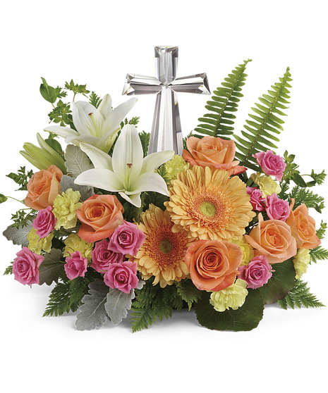 Orange roses, orange gerbera, pink spray rose, white lilies, yellow mini carnations, bupleurum, dusty millers, flat fern, and salal are arranged around the crystal cross 
