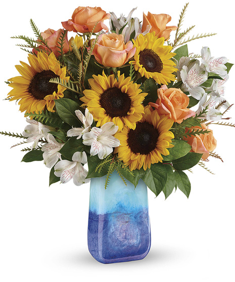 dark blue at bottom lighter blue on top handblown vase with sunflowers in center, orange roses, white alstro, lemon leaf & gravellia