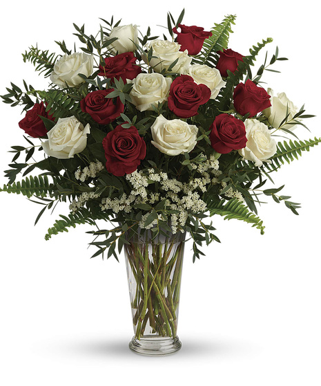 red and white roses with salal, eucalyptus, and fern in clear glass vase with white filler flowers