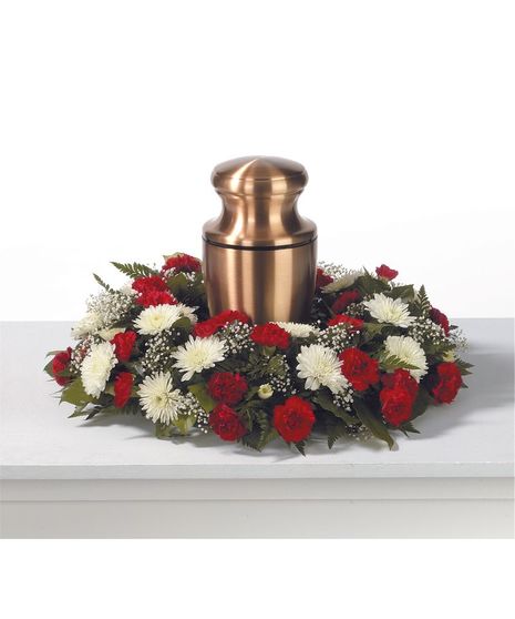  A ring of made with red mini carnations, white cushions, baby's breath, salal and leather leaf displayed around a copper urn(not included)