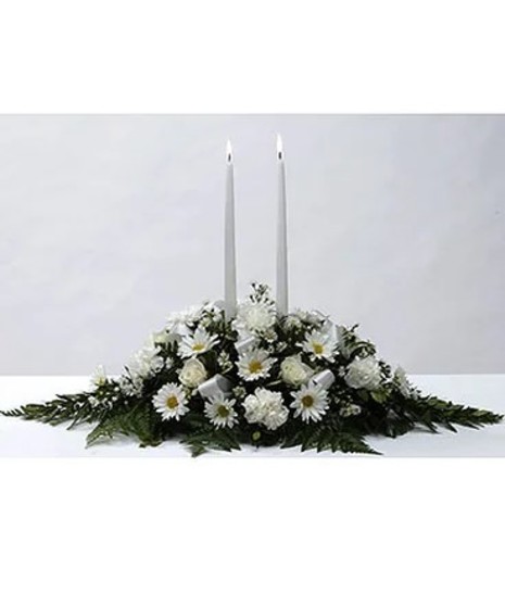2 white taper candle centerpiece set amongst lush leather leaf and white carnations, daisies and roses in a design dish