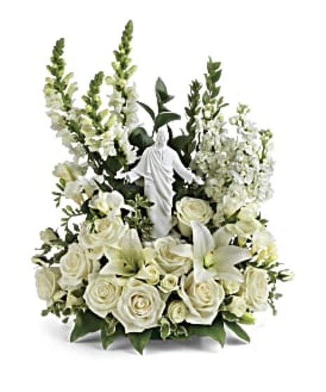 jesus statue in center with white and craeam roses, spray roses, stock, snap dragons, lilies and salal and ruscus in a three sided arrangement 