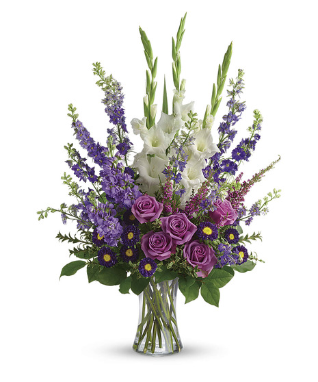 clear vase with tall arrangement of white gladiola,lavender roses and larkspur, purple aster and salal and pittosporum