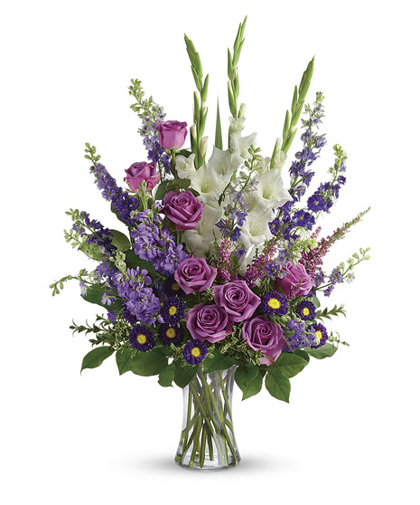 clear vase with tall arrangement of white gladiola,lavender roses and larkspur, purple aster and salal and pittosporum