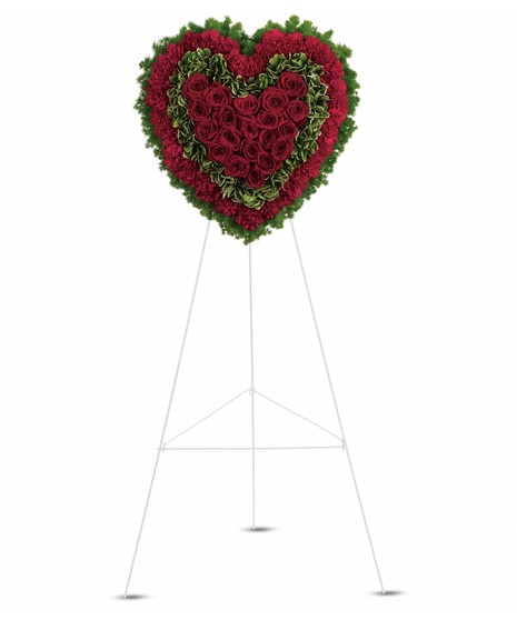 solid heart with red roses in center surrounded by pittosporum surrounded by ring of red carnations and finished with final outer layer of green fern on green easel