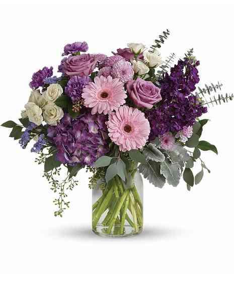 Clear vase with pink gerbera, lavender roses & buttons, purple hydrangea, stock, carnations, white spray roses, purple statice, dusty miller, spiral and seeded eucalyptus