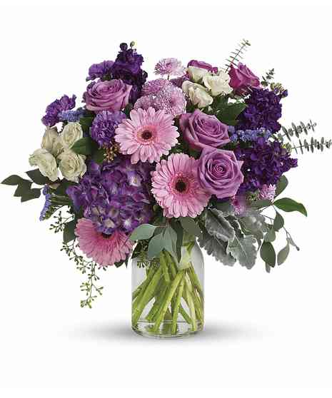 Clear vase with pink gerbera, lavender roses & buttons, purple hydrangea, stock, carnations, white spray roses, purple statice, dusty miller, spiral and seeded eucalyptus
